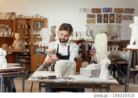 Stone carver works with wooden hammer and chisel at limestone. 108210318