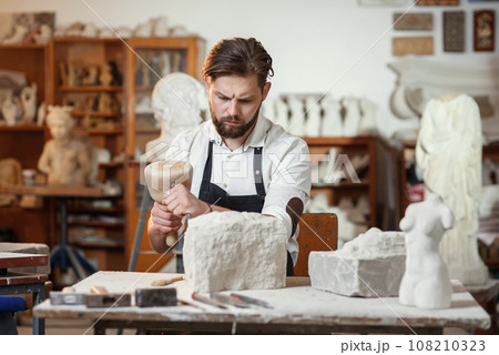 Stone carver works with wooden hammer and chisel at limestone. 108210323
