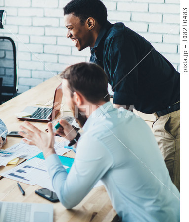 Positive adult multiracial office workers joking while sharing ideas during meeting in light modern conference room 108210483