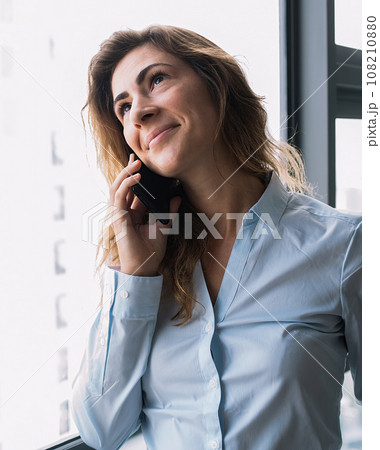 Content lady having conversation on phone nearby window 108210880