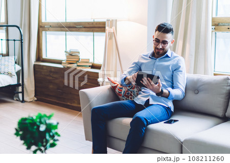 Modern guy and lady using electronic devices sitting across each other in light apartment 108211260