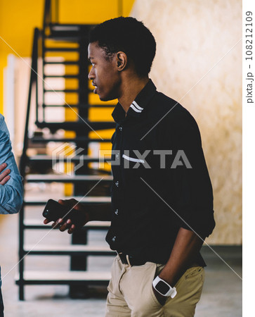 Calm pensive man listening attentively to African American friend while having interesting conversation in corridor of modern building in daytime Calm pensive man listening attentively to African American friend while having interesting conversation in corridor of modern building in daytime 108212109