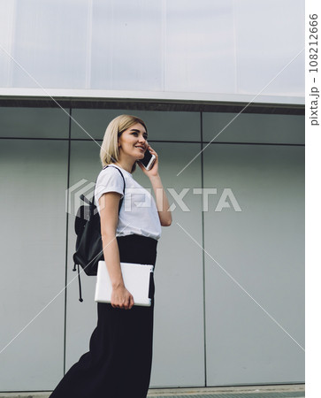 Cheerful adult blond female talking on smartphone in downtown Cheerful adult blond female talking on smartphone in downtown 108212666