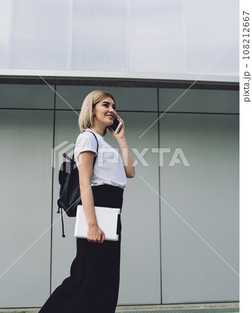 Cheerful adult blond female talking on smartphone in downtown Cheerful adult blond female talking on smartphone in downtown 108212667