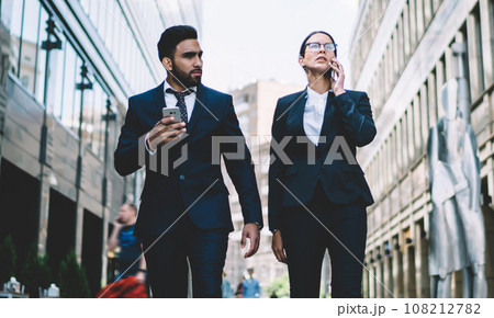 Content business partner walking in downtown street with smartphone 108212782