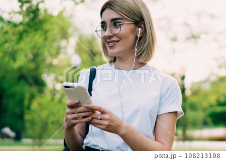 Smiling female with earphones and smartphone in park 108213198