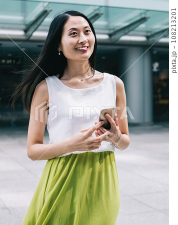 Cheerful Asian woman texting on phone 108213201