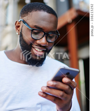 Positive millennial man chatting online on smartphone spending time outdoors in urban setting, 108213292