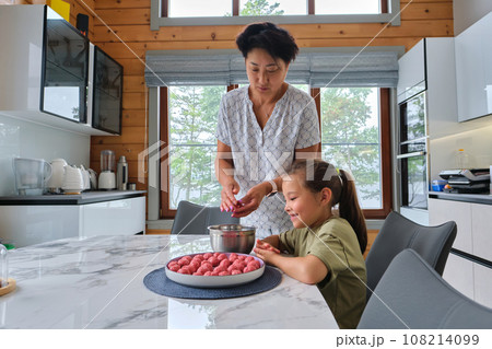 Grandmother and granddaughter preparing meatballs. 108214099
