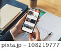 Businessman hand holding black smartphone with reading online news on website on desk in the office. 108219777