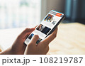 Businessman hand holding black smartphone with reading online news on website on desk in the office. 108219787