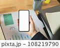 Businessman hand holding black smartphone with blank screen on desk in the office. 108219790