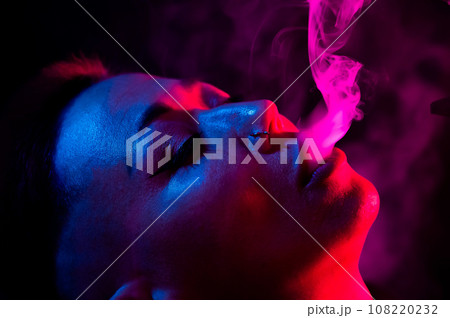 Portrait asian woman with shaved temples smokes vape in neon light. Portrait asian woman with shaved temples smokes vape in neon light. 108220232