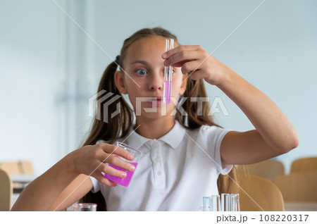 A schoolgirl conducts experiments in a chemistry lesson. Girl pouring colored liquids from a beaker.  108220317