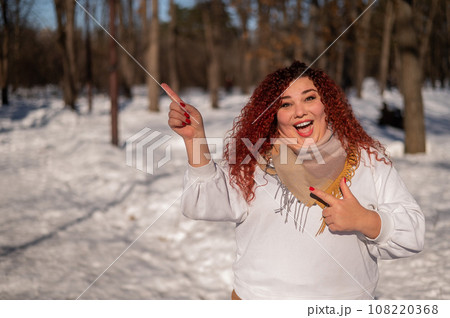 A chubby red-haired woman in a white sweatshirt. Girl fooling around in the park in winter.  A chubby red-haired woman in a white sweatshirt. Girl fooling around in the park in winter.  108220368
