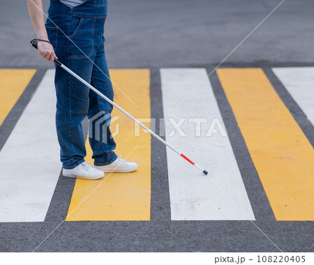 Close-up of the legs of a blind woman crossing the road at a crosswalk with a cane.  108220405