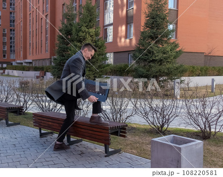 Caucasian man freaks out and breaks laptop outdoors. Caucasian man freaks out and breaks laptop outdoors. 108220581