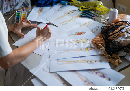 Faceless woman draws sketches of swimwear with a pencil. Close-up of the hands of a fashion designer. 108220734