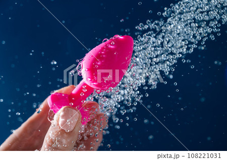 Woman washing pink anal plug under shower on blue background. Woman washing pink anal plug under shower on blue background. 108221031