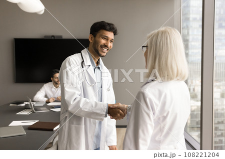 Happy young Indian doctor in white uniform coat shaking hands 108221204