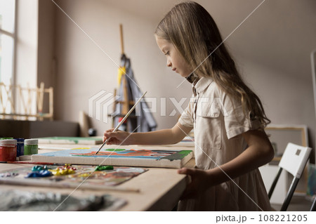 Serious concentrated girl painting on canvas with acrylic paints 108221205