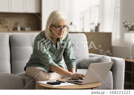 Serious blonde elderly woman in glasses doing domestic financial work 108221221