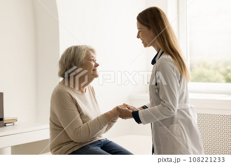 Woman therapist in coat holding hands of elderly female patient 108221233