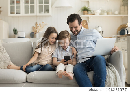 Father and little children using smartphone and laptop Father and little children using smartphone and laptop 108221377