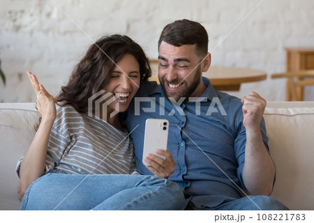 Happy excited adult dating couple using smartphone, staring at screen Happy excited adult dating couple using smartphone, staring at screen 108221783