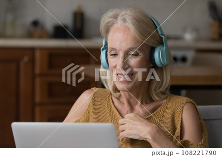 Positive laptop user woman in big wireless headphones watching webinar Positive laptop user woman in big wireless headphones watching webinar 108221790