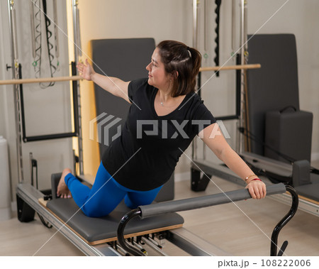 Overweight caucasian woman doing pilates exercises on a reformer.  108222006