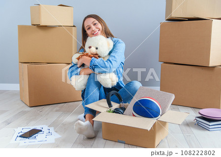 Beautiful smiling girl puts on the headphones on the teddy bear toy and sitting on the floor in the empty new apartment. Beautiful smiling girl puts on the headphones on the teddy bear toy and sitting on the floor in the empty new apartment. 108222802