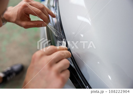 Worker detailer cutting off excess of polymer protective outer coating closeup Worker detailer cutting off excess of polymer protective outer coating closeup 108222904