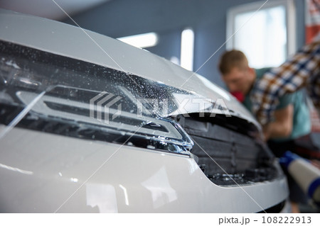 Technician covering car body with protective film at vehicle detailing service Technician covering car body with protective film at vehicle detailing service 108222913
