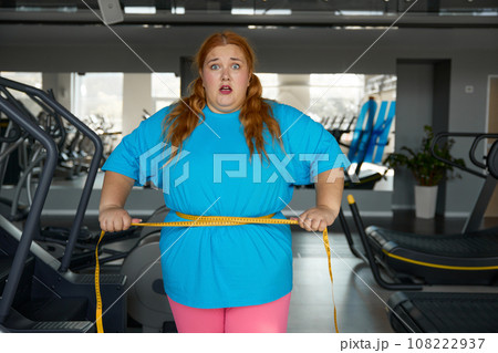 Portrait cute woman with excess weight ties herself with measuring tape 108222937