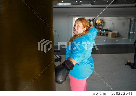 Concentrated fat woman using boxing gloves doing punching exercises Concentrated fat woman using boxing gloves doing punching exercises 108222941