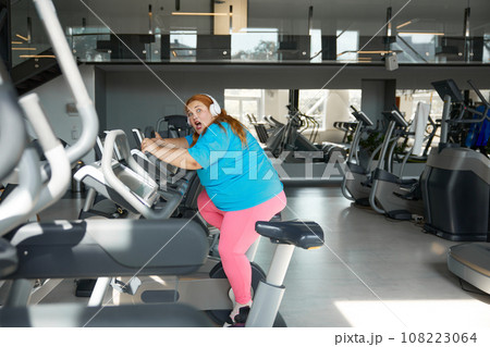 Crazy motivated overweight woman riding fast on stationary bike Crazy motivated overweight woman riding fast on stationary bike 108223064