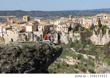 Woman tourist takes pictures of the picturesque houses on the cliff edge of the city of Cuenca Woman tourist takes pictures of the picturesque houses on the cliff edge of the city of Cuenca 108223415