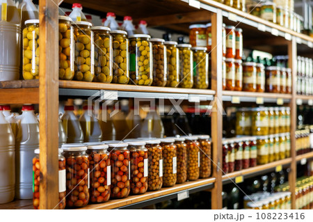 Marinated whole unpitted green olives in jars on shelf rack in store 108223416