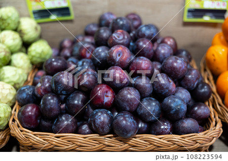 Ripe juicy plums in wicker box on supermarket shelf 108223594