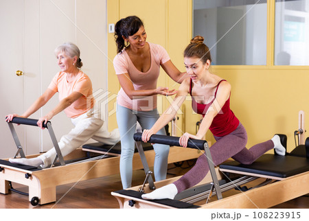 Hispanic female pilates instructor helping girl exercising on reformer 108223915
