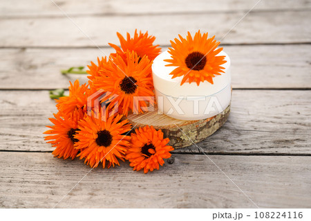 Medical Dermatology. Cosmetic cream for cleansing the skin with calendula flowers. Cream for body care with calendula. Fresh orange calendula flowers on a wooden background in nature. Medical Dermatology. Cosmetic cream for cleansing the skin with calendula flowers. Cream for body care with calendula. Fresh orange calendula flowers on a wooden background in nature. 108224116