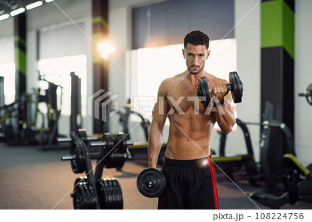 Attractive fitness man working out with dumbbells during training biceps in the gym. Sporty and healthy concept. Attractive fitness man working out with dumbbells during training biceps in the gym. Sporty and healthy concept. 108224756