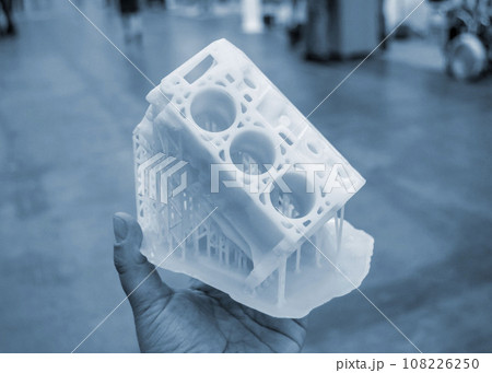 Person holding in palm of hand prototype of car engine printed on 3D printer from molten white plastic. Three-dimensional model. Additive progressive modeling technology. Modern new printing industry. Person holding in palm of hand prototype of car engine printed on 3D printer from molten white plastic. Three-dimensional model. Additive progressive modeling technology. Modern new printing industry. 108226250