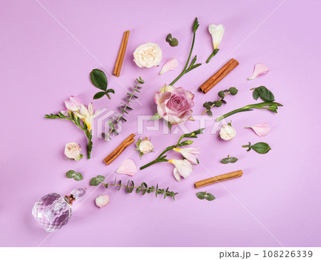 Beautiful flat lay composition with bottle of perfume, cinnamon and flowers on lilac background Beautiful flat lay composition with bottle of perfume, cinnamon and flowers on lilac background 108226339