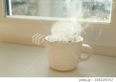Cup of hot drink near window on rainy day 108226352