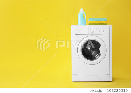 Modern washing machine with stack of towels and detergent on yellow background, space for text. Laundry day 108226359