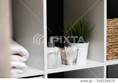 Dispenser, cotton swabs and plant on white shelf in bathroom Dispenser, cotton swabs and plant on white shelf in bathroom 108226678