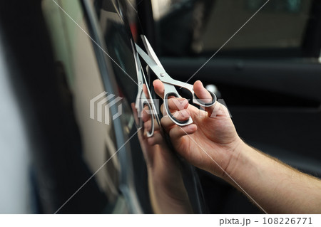 Worker tinting car window with foil in workshop, closeup Worker tinting car window with foil in workshop, closeup 108226771