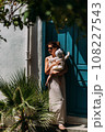 A stylish woman with a baby in her arms. A baby in his mother's arms. A beautiful portrait of a child in the arms of his mother. Mom hugs the baby. A woman with a baby on the background of the door 108227543
